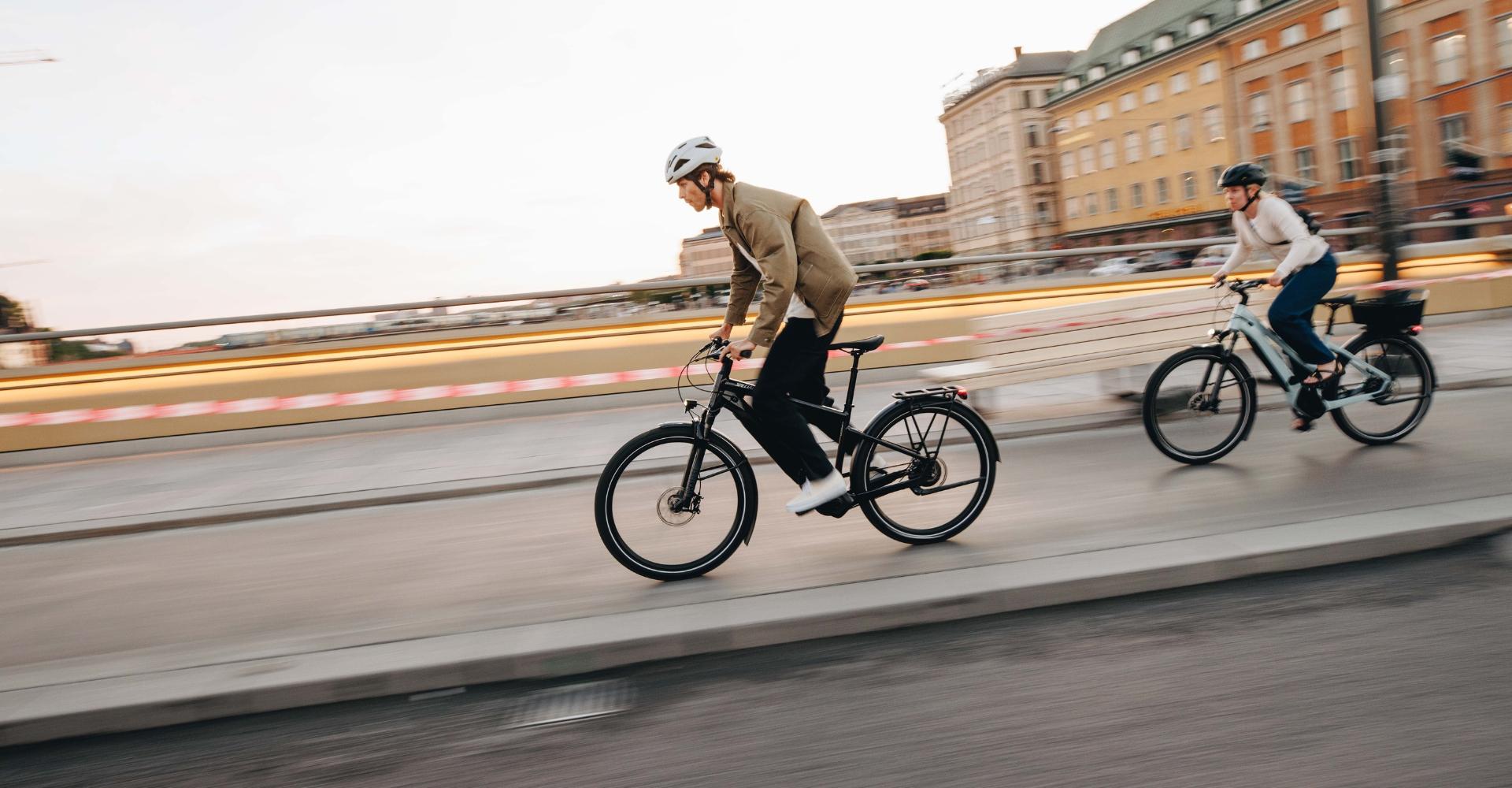 Zwei Personen fahren auf e-Bikes durch eine urbane Gegend