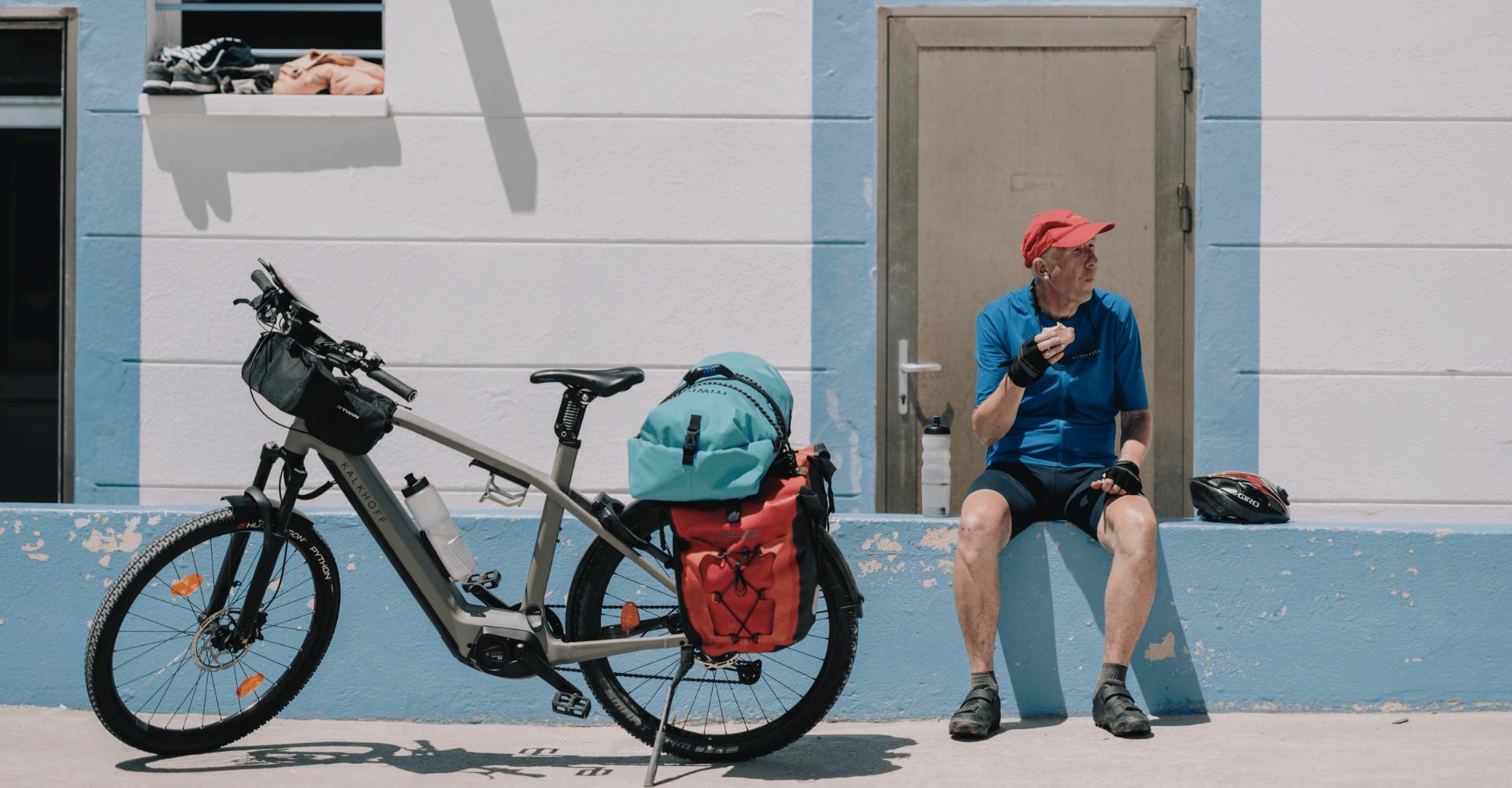 Ein Mann sitzt auf einer Mauer und isst, vor ihm sein Kalkhoff e-Bike