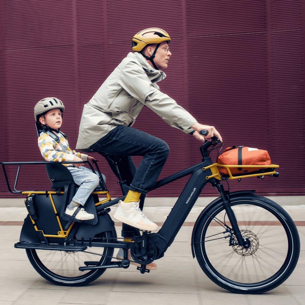 Ein Mann fährt auf dem Riese und Müller Multicharger und einem Kind an einer bunten Wand vorbei