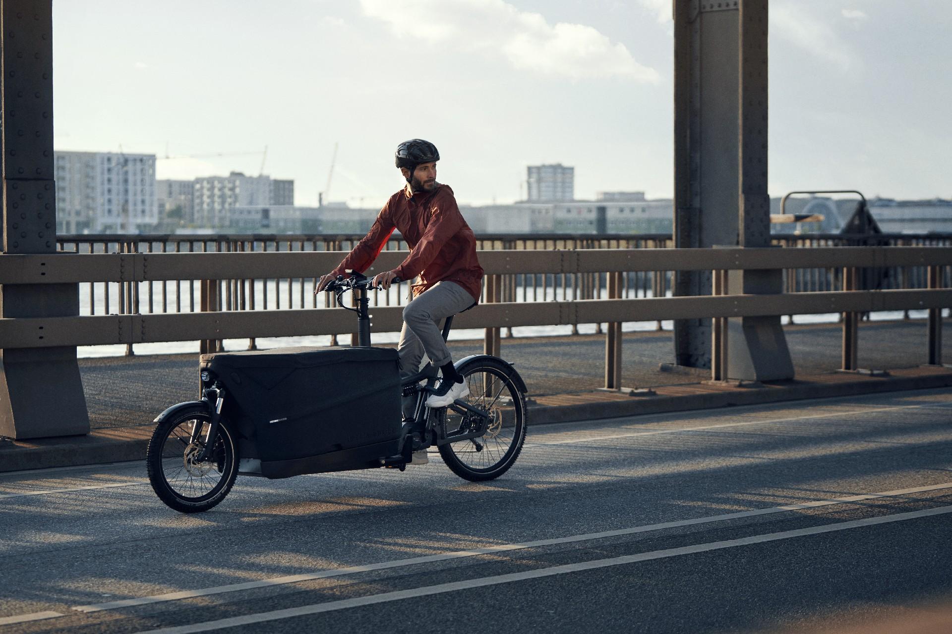 Ein Mann fährt mit einem Riese und Müller Lastenrad über die Brücke