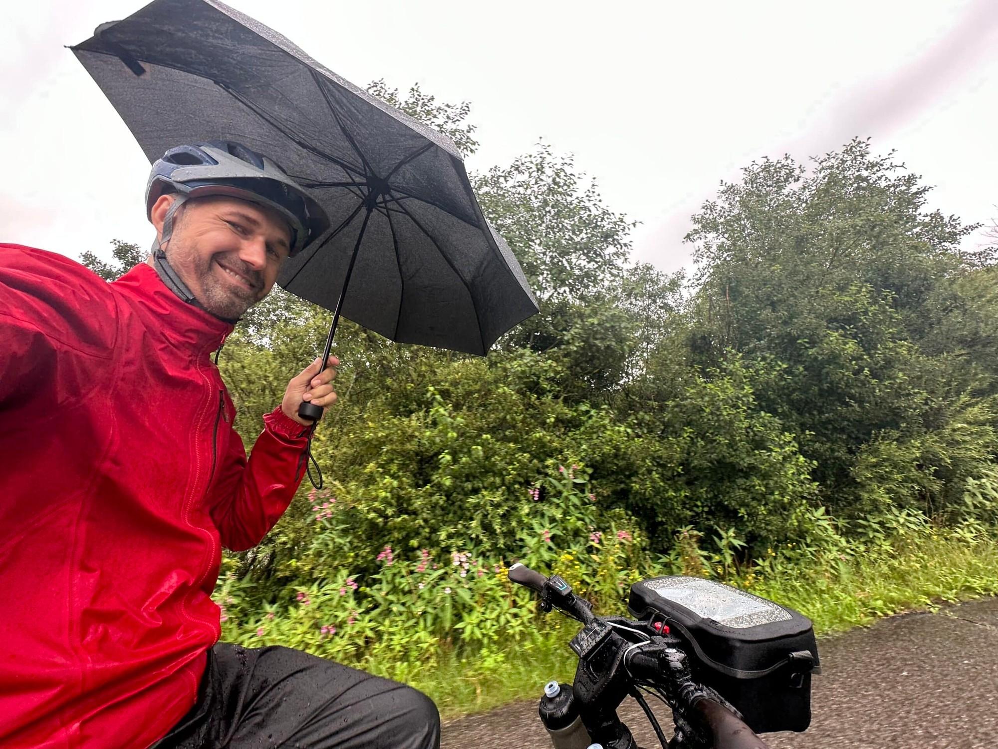 e-Biker mit Regenschirm auf feuchtem Weg