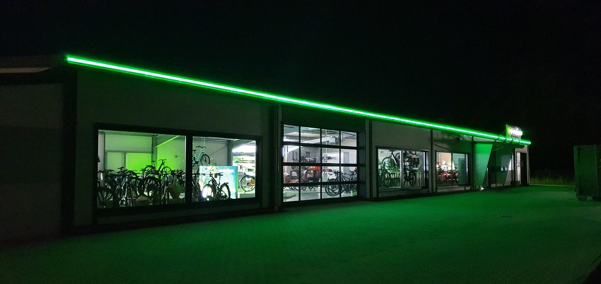 Das Bild zeigt die Außenansicht einer e-motion e-Bike Welt in Schwarzenfeld, beleuchtet von grünem Licht. Die Fassa