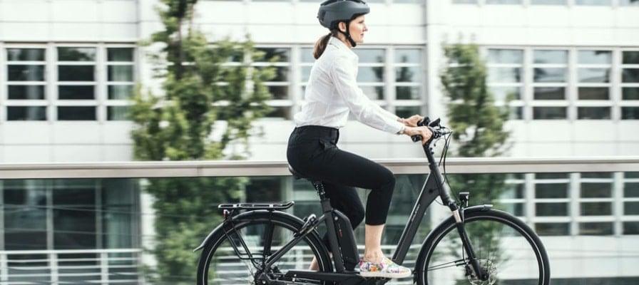 Frau auf E-Bike mit Helm vor Bürogebäude
