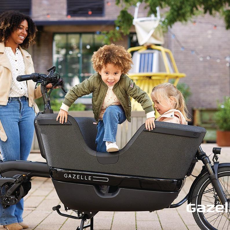 Eine Frau steht vor dem Lastenrad Gazelle Makki, in der Transportbox sitzen zwei Kinder