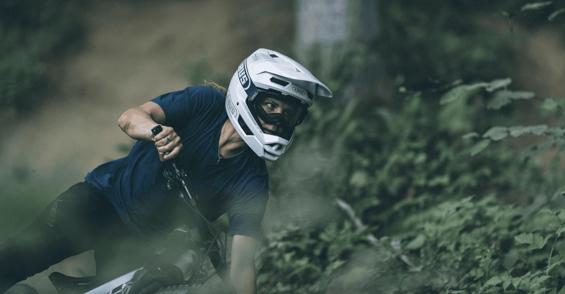 Eine Frau fährt auf einem e-MTB mit einem ABUS Helm durch den Wald