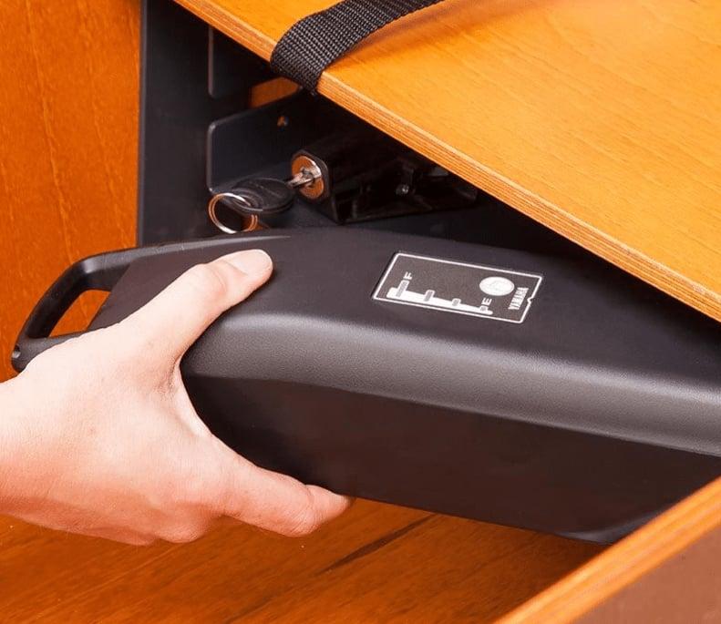 Hand entnimmt schwarzen Akku aus Holzschrank