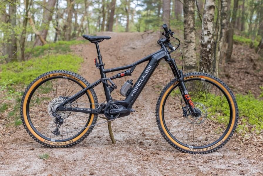 Das Bild zeigt ein Hercules Nos FS 1.1 E-Bike, das auf einem unbefestigten Waldweg positioniert ist.