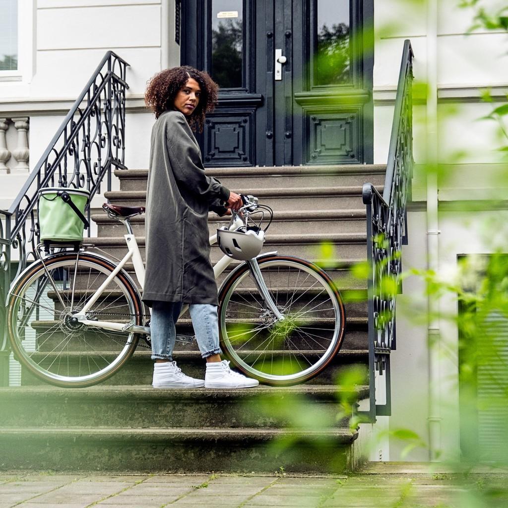 Eine Person mit einem modernen Stadtrad steht vor einer eleganten Haustür. Ideal für urbane Mobilität mit Stil.