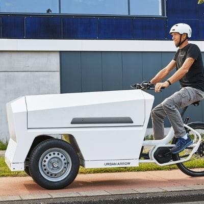 Mann fährt Urban Arrow Lastenrad auf Radweg in städtischer Umgebung