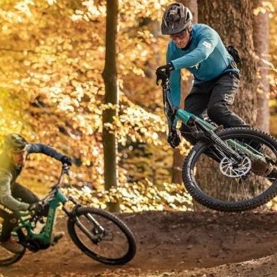 Zwei Mountainbiker im herbstlichen Wald bei Sprung und Abfahrt