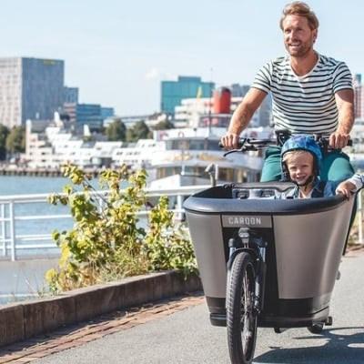 Mann fährt Carqon E-Lastenrad mit Kind auf städtischer Promenade