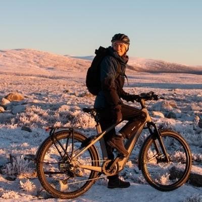 Mann auf E-Bike in verschneiter Landschaft bei Sonnenuntergang