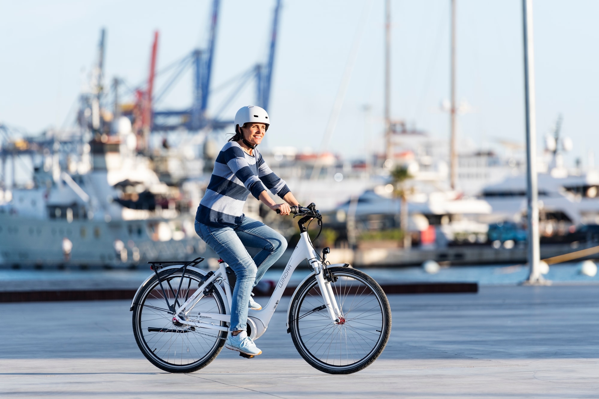 Dame fährt ein Limar Urban-Fahrrad mit Helm am Hafen entlang. Perfekt für stilvolle City-Touren.