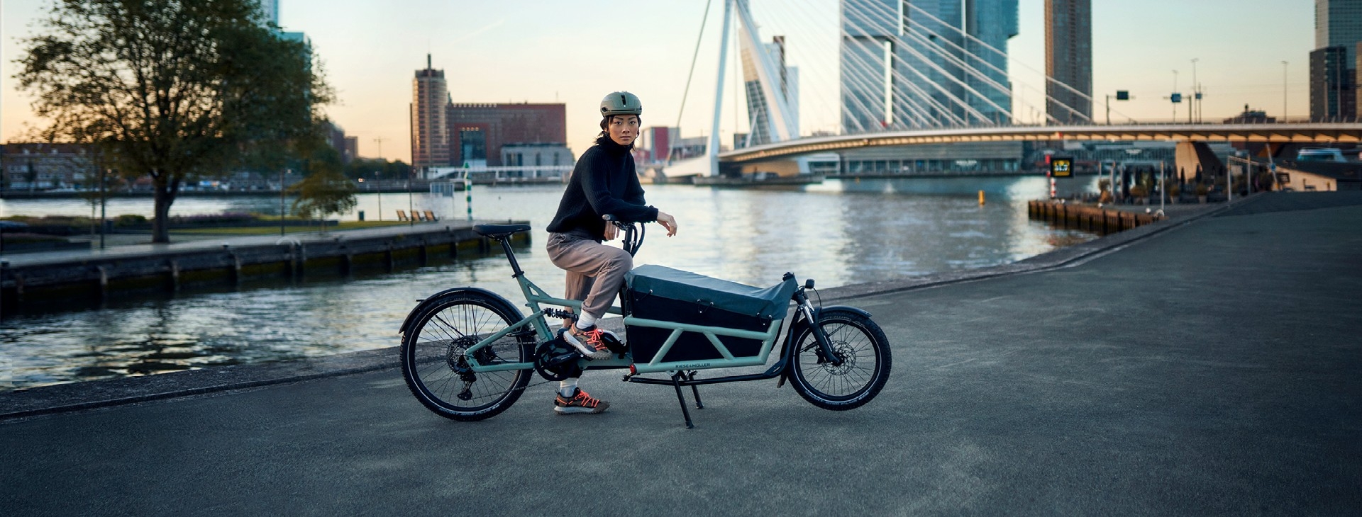 Eine Frau sitzt auf ihrem Riese & Müller Load4 60 Cargo e-Bike und steht vor dem Wasser