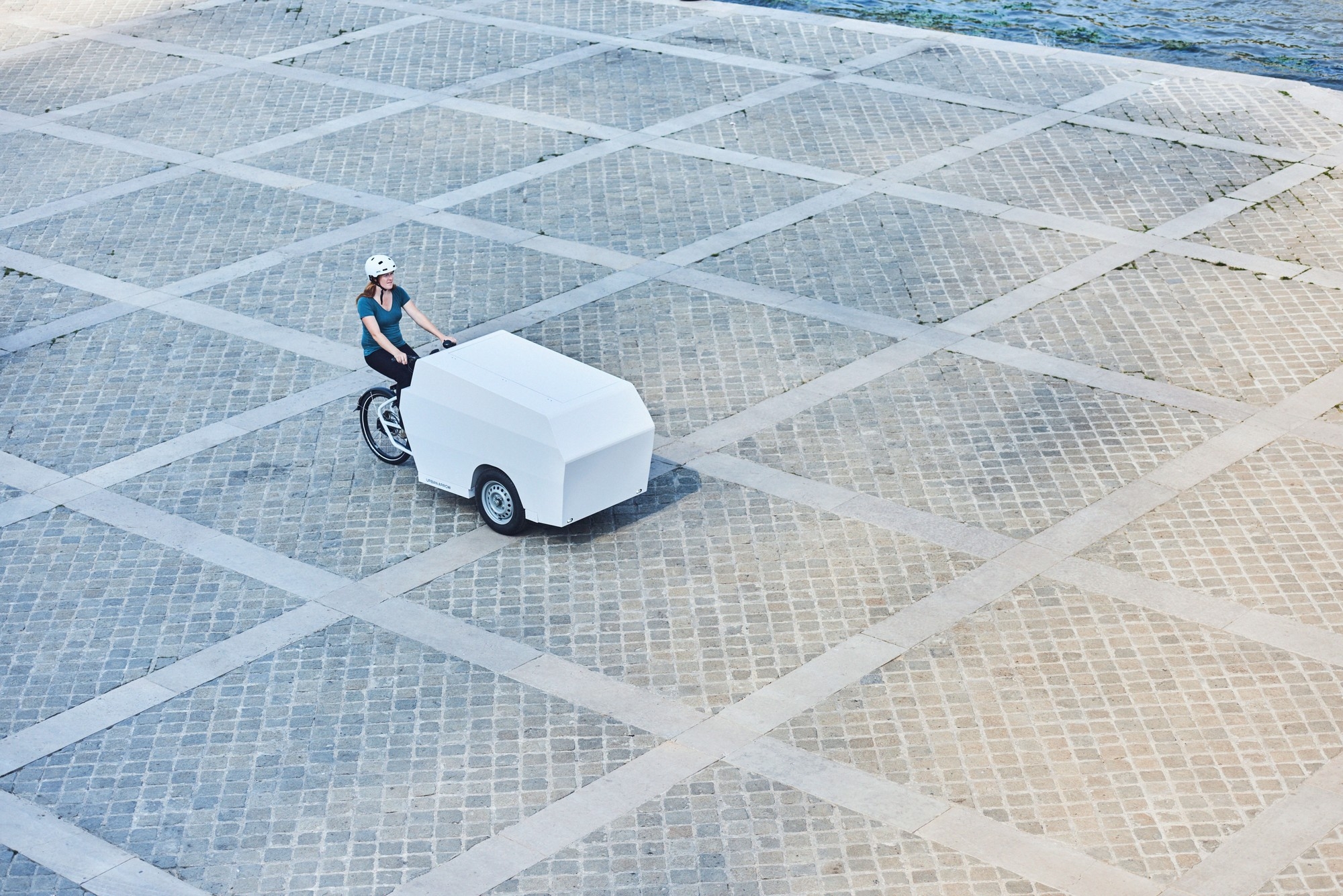 Eine Frau fährt mit dem Lasten e-Bike Tender von Urban Arrow über einen großen Platz