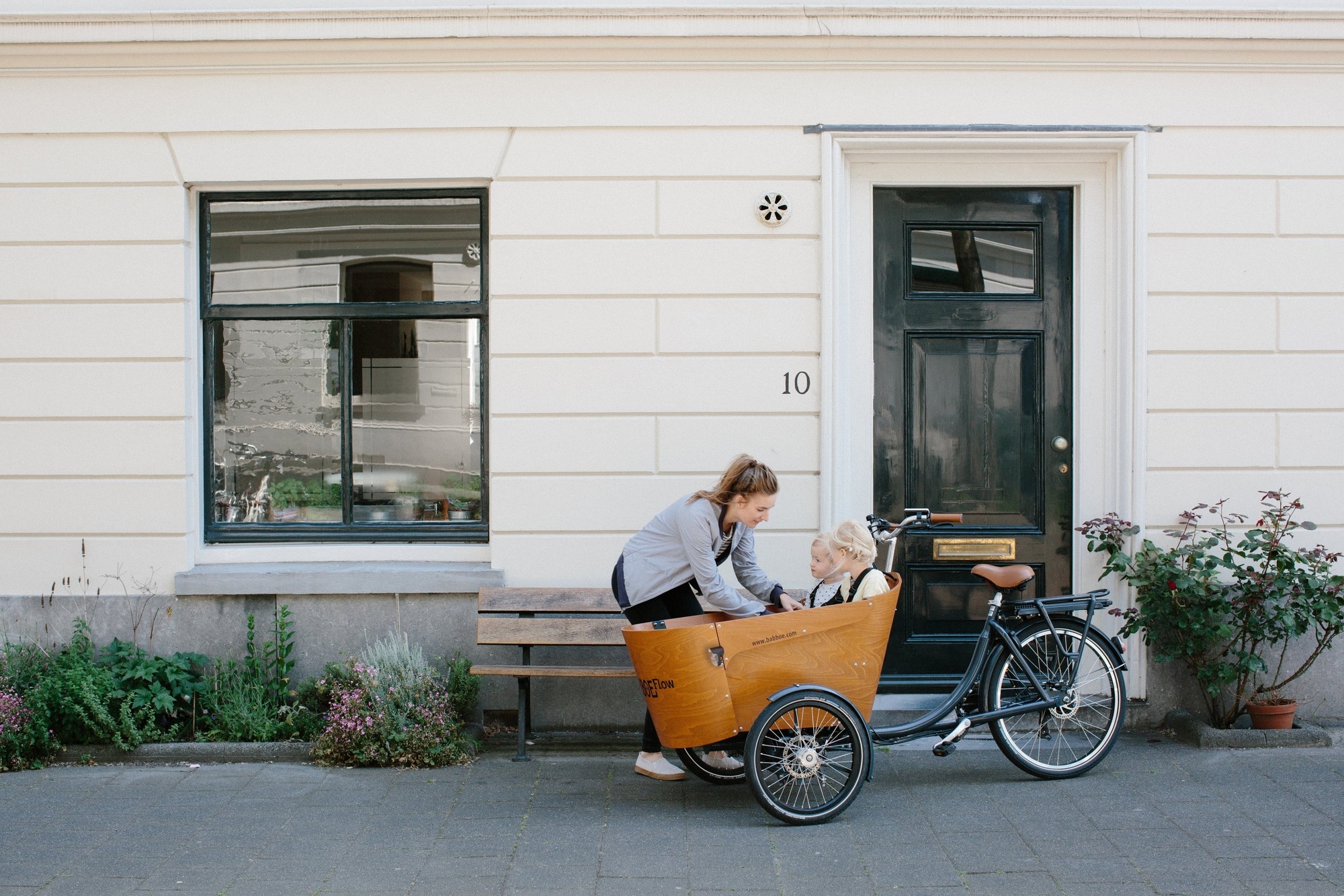 Das Bild zeigt eine moderne städtische Szenerie, in der eine Frau und zwei Kindern mit einem lasten e-Bike steht