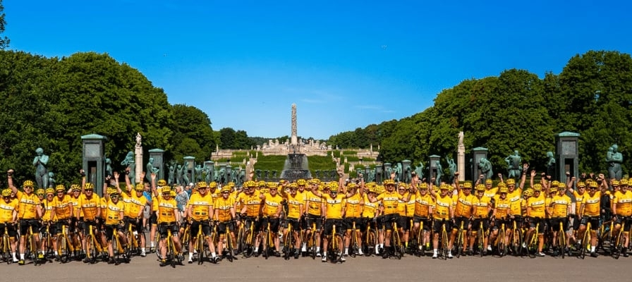 Gruppe von Radfahrern in gelben Trikots vor monumentalem Park