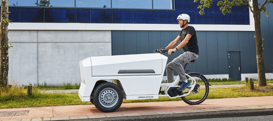 Mann fährt Urban Arrow Lastenrad auf Radweg in städtischer Umgebung