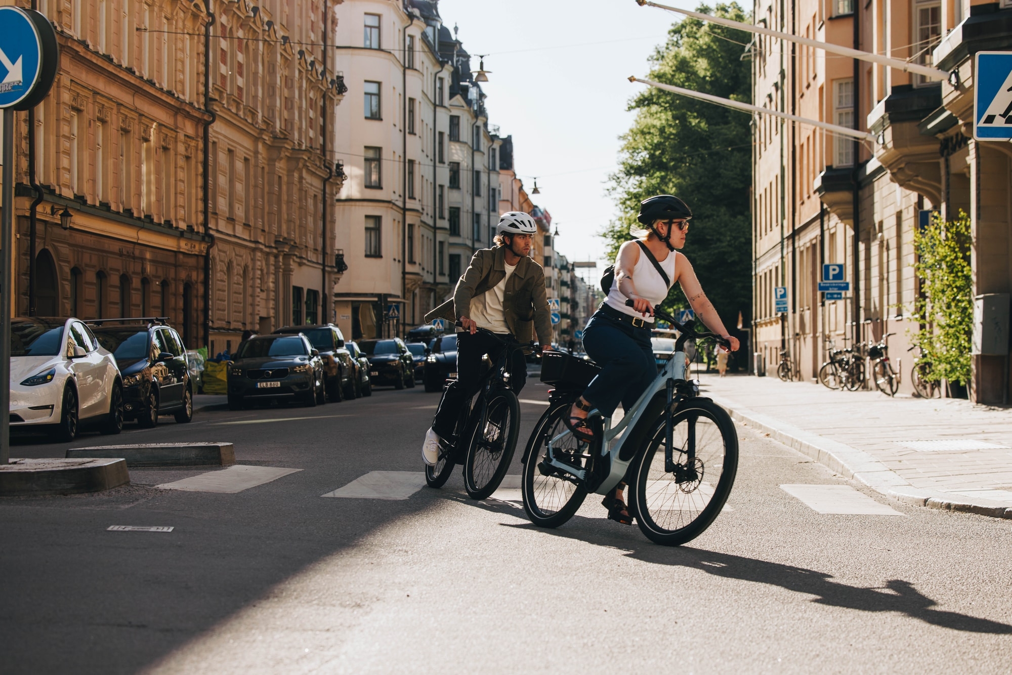 Zwei Personen fahren moderne E-Bikes durch eine sonnige Stadtstraße. Perfekt für urbane Mobilität.