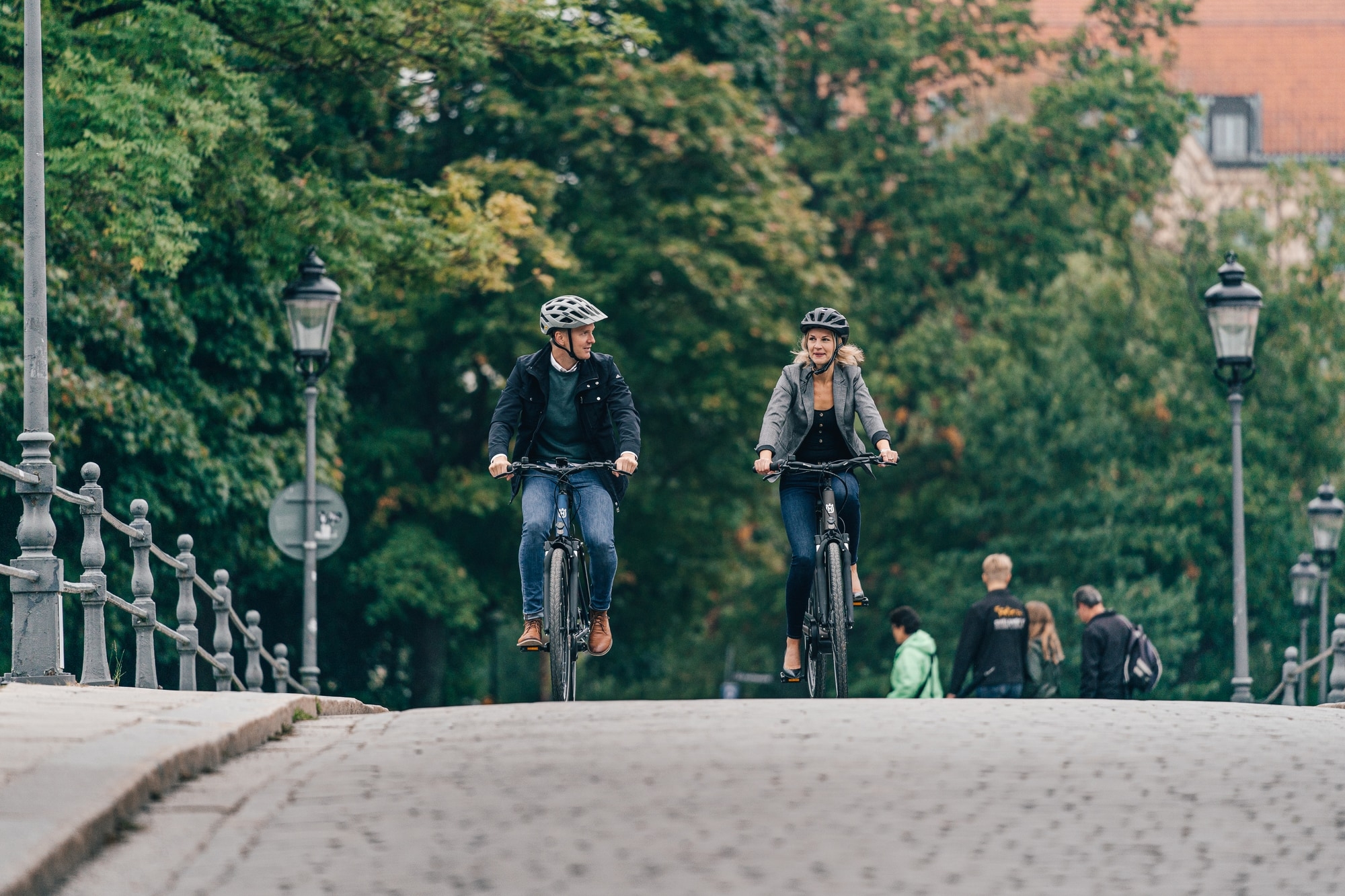 Zwei Personen fahren Eco City E-Bikes auf einer Brücke, umgeben von städtischem Grün.