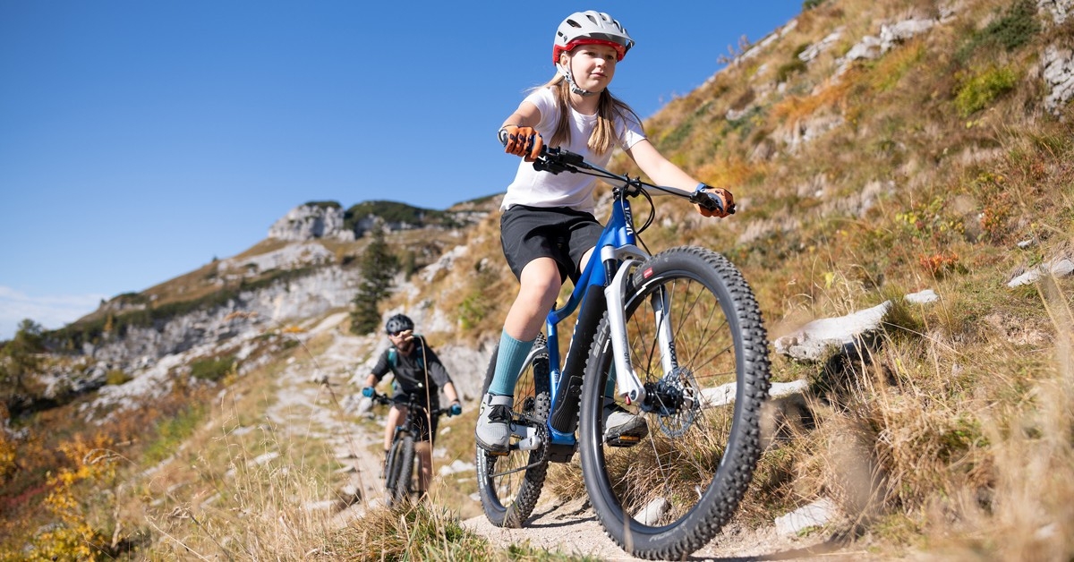Das Bild zeigt zwei junge Radfahrer, die mit einem Woom E-Bike in einem bergigen Gelände fahren.
