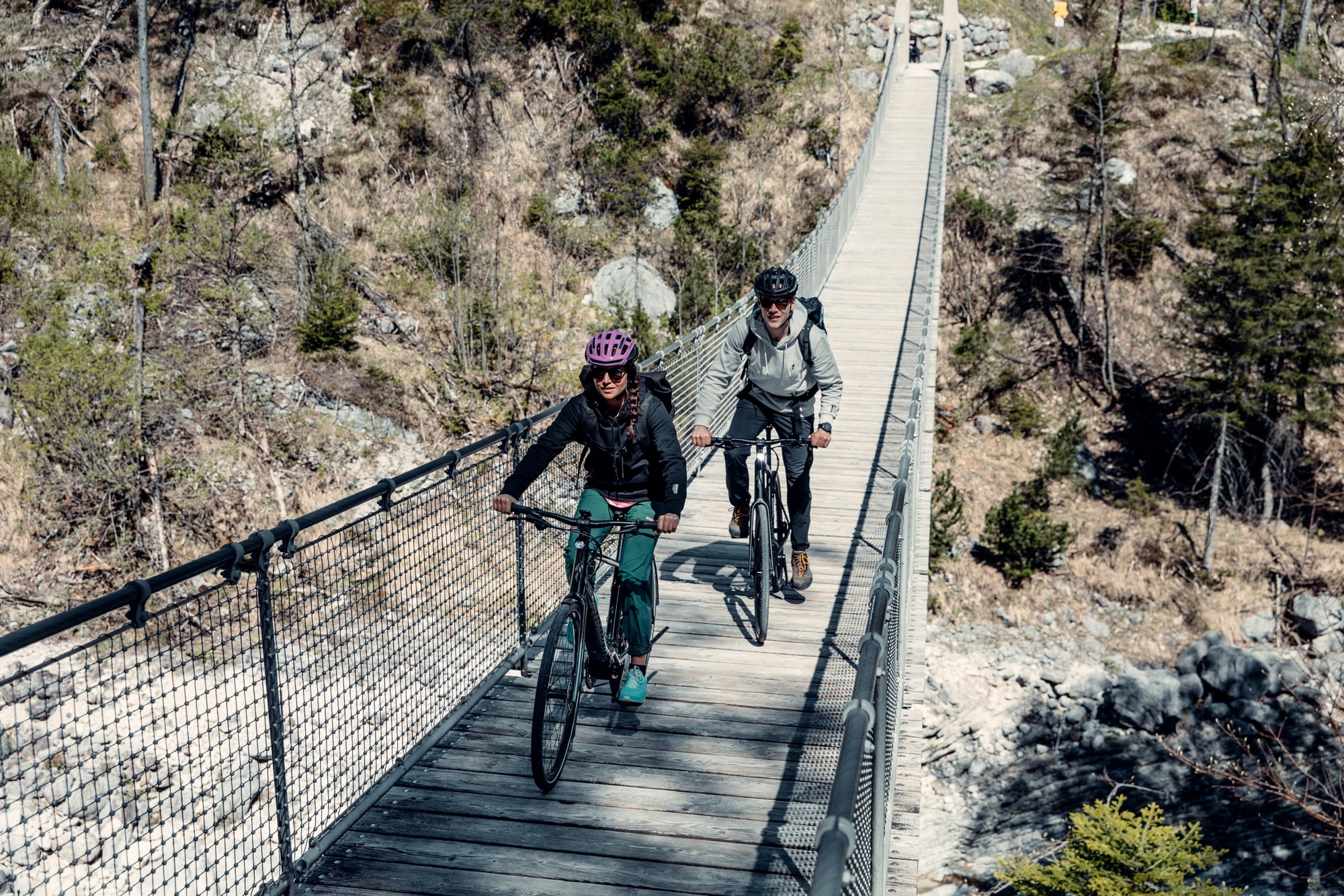 Zwei Radfahrer überqueren eine beeindruckende Hängebrücke inmitten einer malerischen Naturlandschaft. Ideal für abe