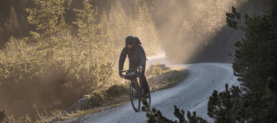 Radfahrer auf Schotterweg im Wald bei Sonnenuntergang