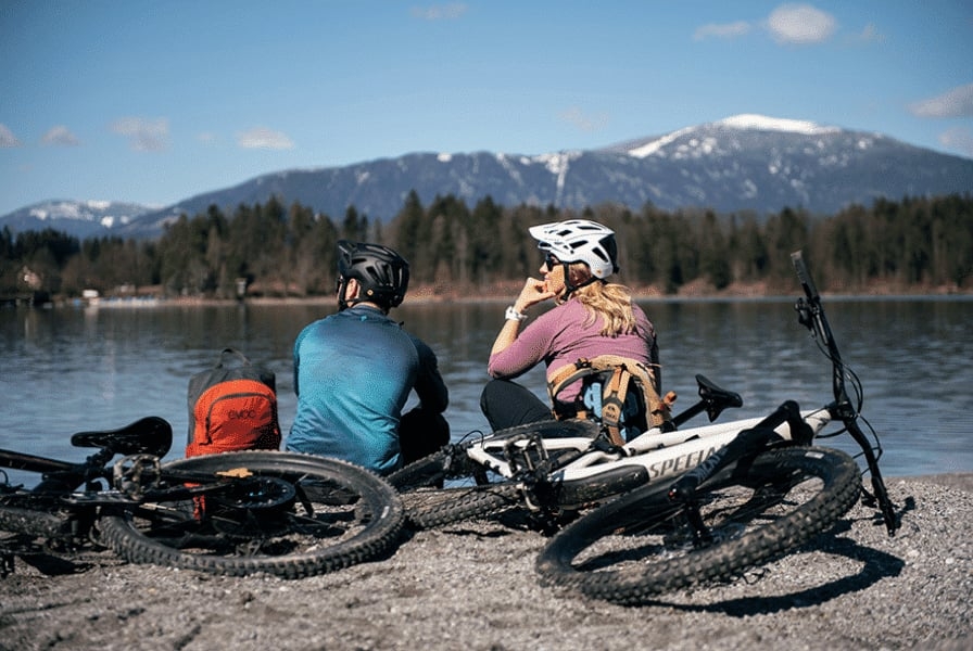 Zwei Radfahrer mit Specialized E-Bikes am Seeufer mit Bergpanorama